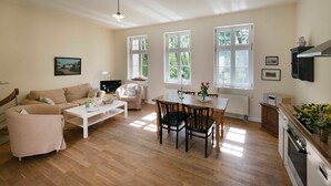 Un salon spacieux comprenant un canapé, une table basse et une table à manger. De grandes fenêtres laissent entrer la lumière naturelle et offrent une vue sur la verdure environnante.