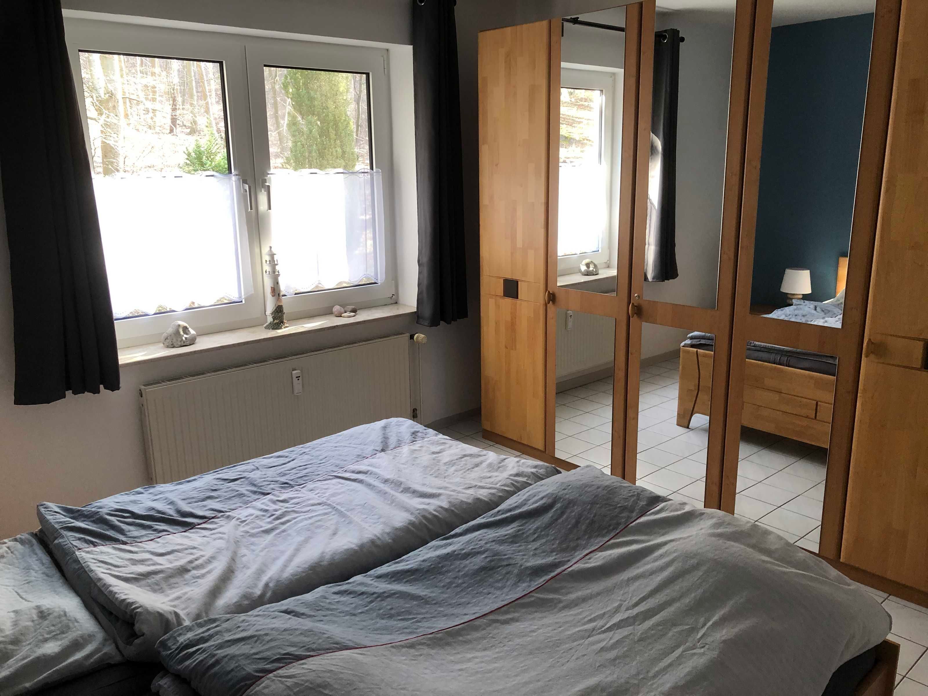 A bedroom with a bed, a window with curtains, a radiator, and a wardrobe with a mirror.