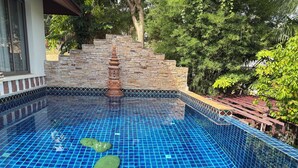 A swimming pool with blue tiles, a stone wall, and a wooden deck. - Private Thai style villa with private  pool (Koh Samui)