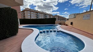Una piscina de borde curvo, rodeada por un paseo de ladrillo y un seto bajo.