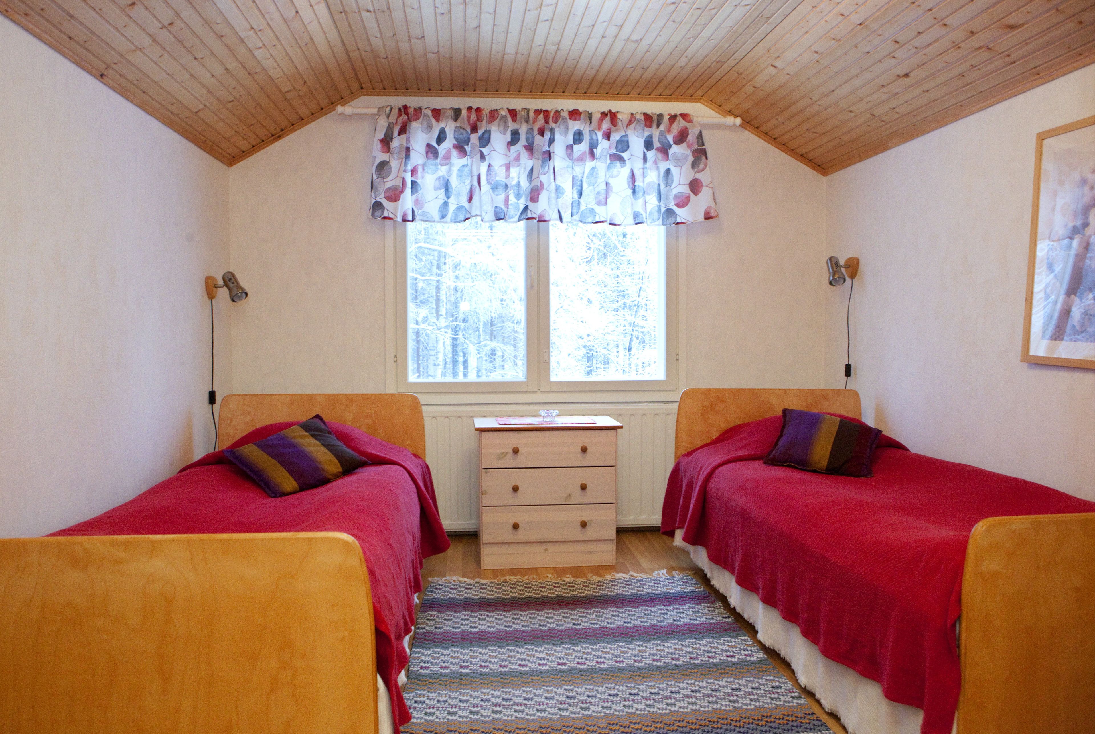 Une chambre avec deux lits, une fenêtre avec des rideaux, un radiateur et un plafond en bois.