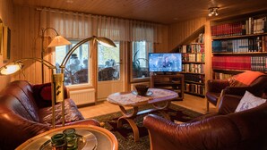 Un salon chaleureux avec des canapés en cuir, une table basse, une bibliothèque et un téléviseur.