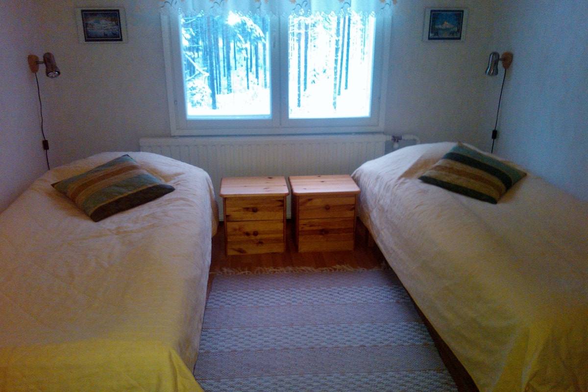 A twin bedroom with two beds, a window with a view of trees, and a radiator.