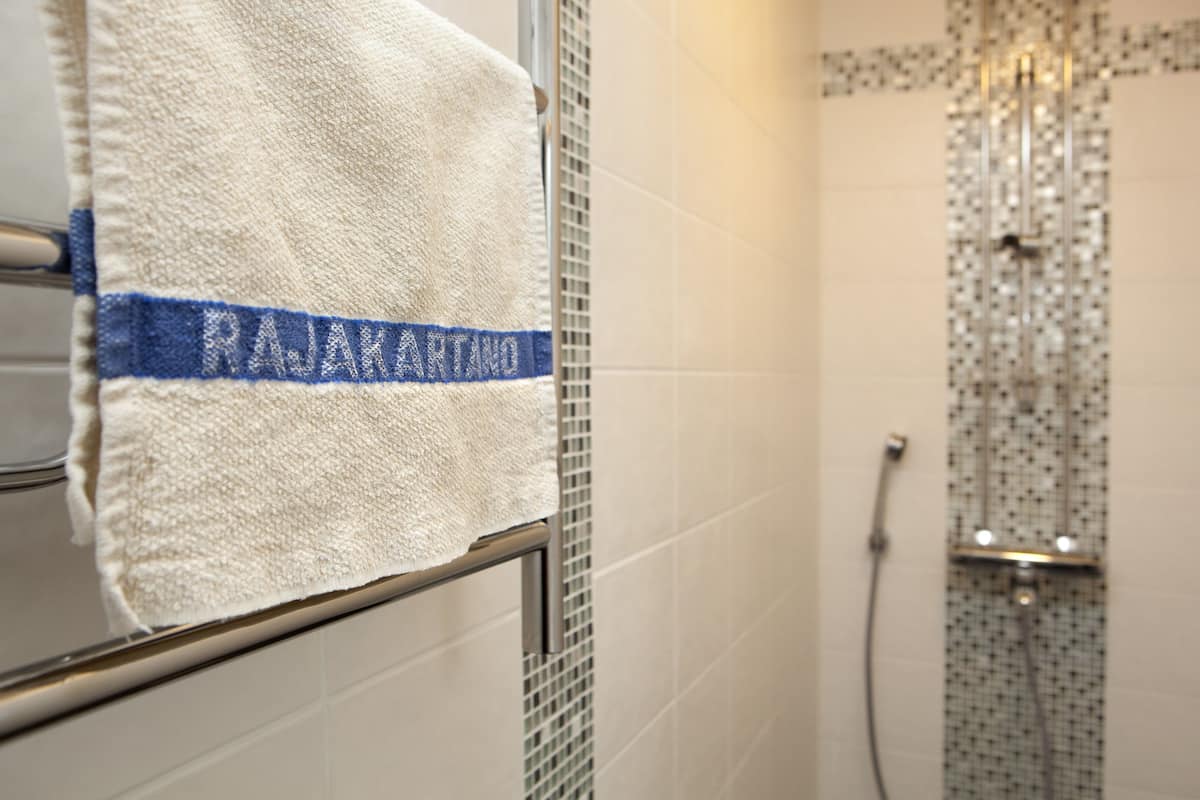A bathroom with a towel rack, a shower with a patterned wall, and a visible water control panel.