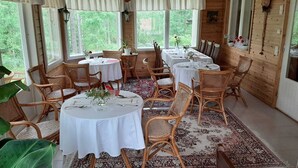 Un espace repas avec des tables rondes et des chaises en osier, de grandes fenêtres et un intérieur en bois.