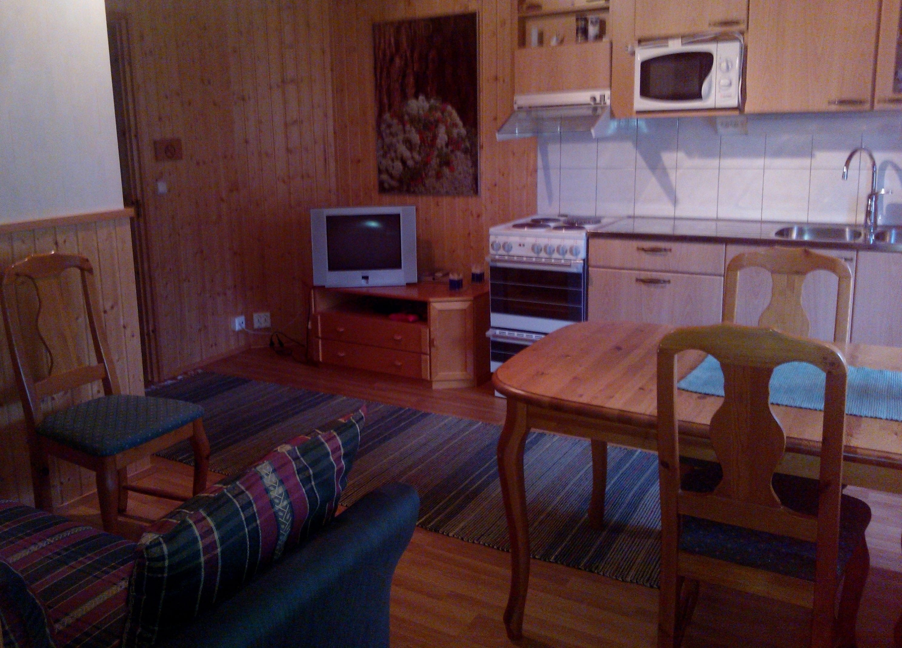 Un espacio habitable compacto con kitchenette, televisor, sofá y mesa de comedor.