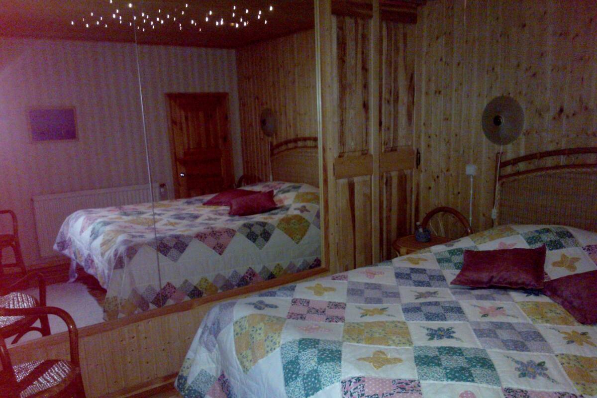 A room with two beds, wooden walls, a chair, and a mirror.