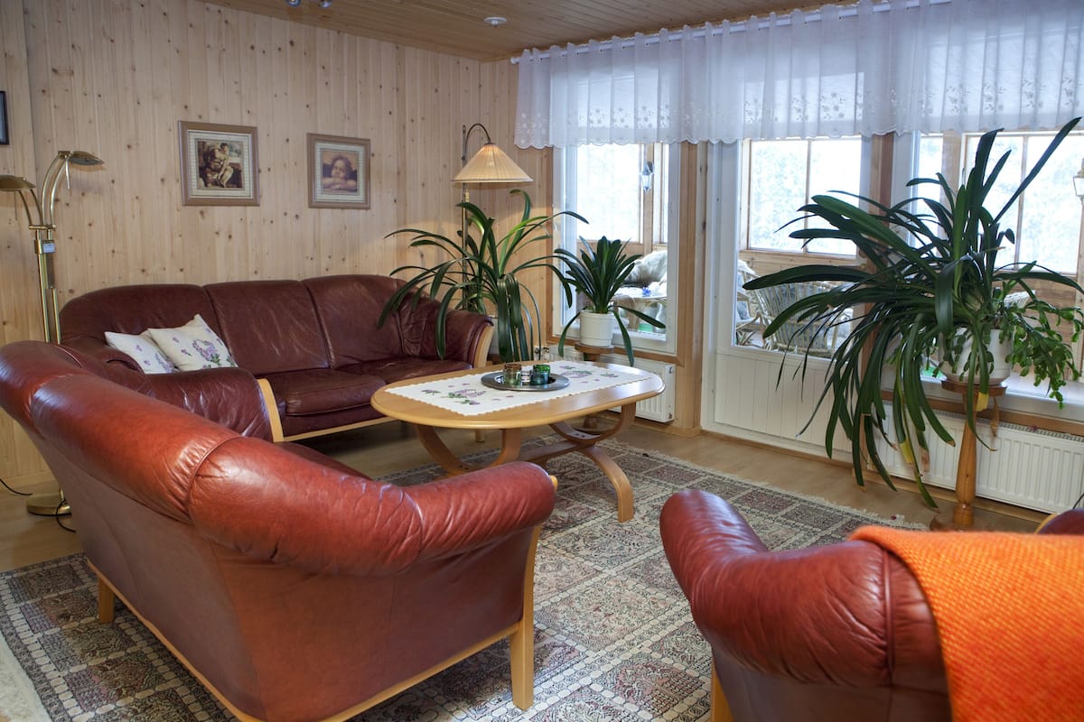 A living room with a brown leather sofa, a wooden coffee table, and two potted plants.