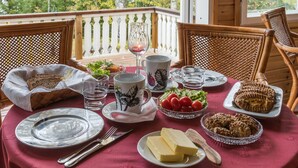 Une table à manger dressée avec des assiettes, des verres et de la nourriture, sur un balcon offrant une vue sur les arbres.