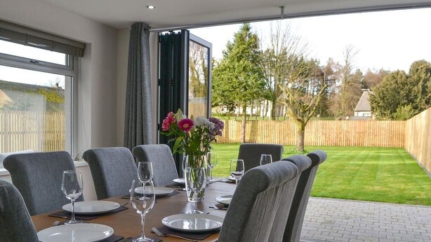 Un área de comedor al aire libre con una mesa preparada para cuatro, rodeada de sillas y un jarrón de flores sobre la mesa.