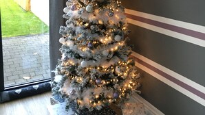 Un árbol de Navidad con luces y adornos, ubicado en una esquina con una ventana y una pared a rayas.