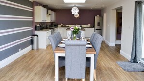 Una cocina moderna con una isla central, un comedor con mesa dispuesta para cuatro personas y una sala de estar con sofá y televisor.