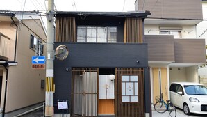 A two-story building with a dark facade, a visible entrance with a sliding door, and a bicycle parked outside. - Chika Ichiyin (Kyoto)