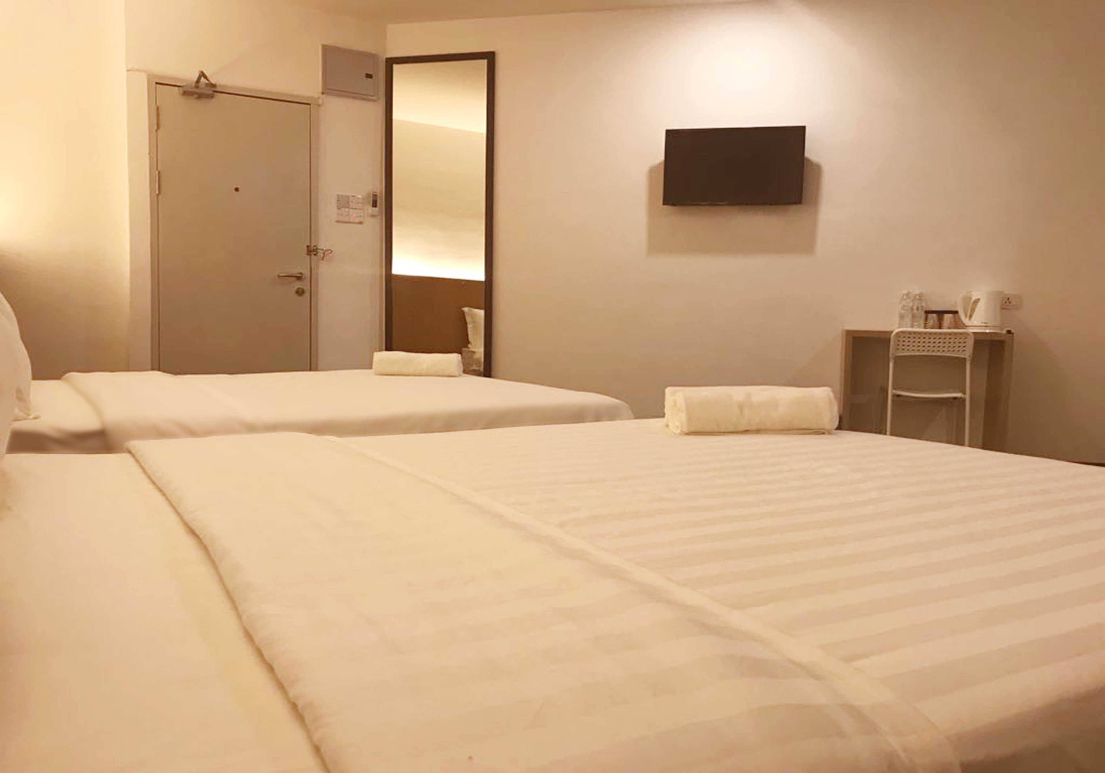 Ein Hotelzimmer mit zwei Betten, einem Fernseher, einem Spiegel, einer Tür und einem kleinen Regal mit Wasserkocher und Tassen.