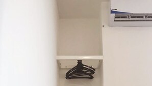 A small room with a wooden table, two water bottles, a kettle, a remote control, and a white chair. There is a black hanger on a white shelf above the table. - Place2Stay Business Hotel @ Metrocity (Kuching)