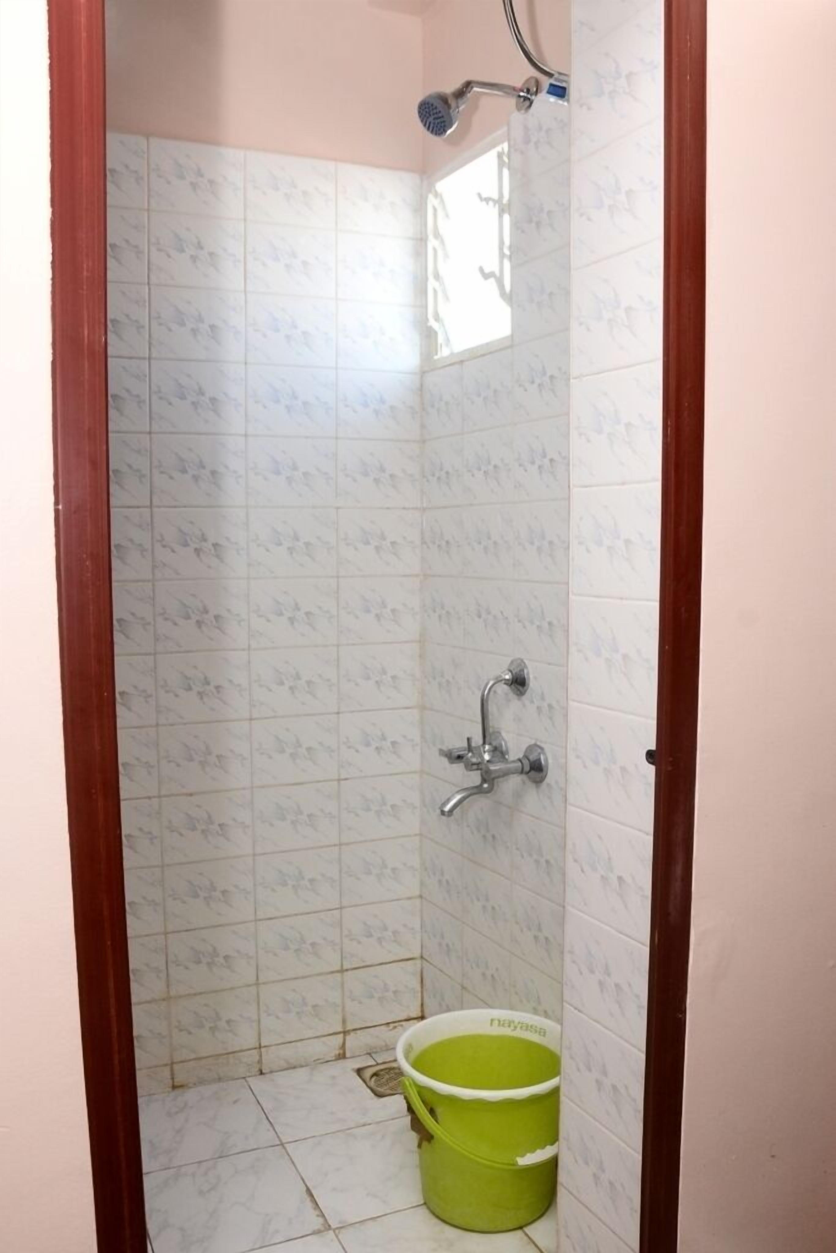 A small bathroom with white tiled walls, a shower, and a green bucket.