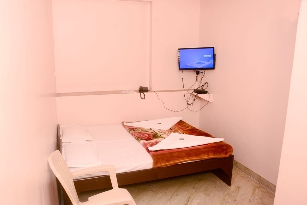 A small, single-bed room with a television mounted on the wall, a chair, and a bedside table.