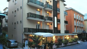 A multi-story hotel with balconies, outdoor seating, and a covered entrance. - Hotel Tre Grazie (Rimini)