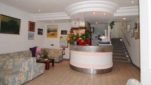 A lobby with a reception desk, a sofa, and a staircase leading to upper floors. - Hotel Tre Grazie (Rimini)