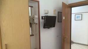 A room with a wooden door, a small wooden cabinet, a wall-mounted television, and a framed picture. - Hotel Tre Grazie (Rimini)
