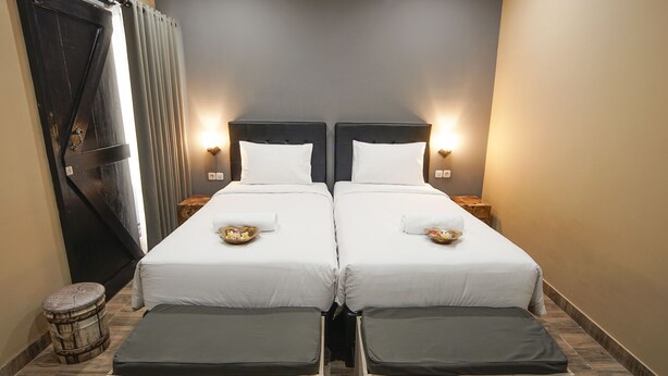 Habitación de hotel con dos camas, cada una con ropa blanca y almohadas, y mesitas de noche con lámparas.