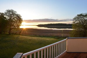 Une terrasse donnant sur un lac, bordée d’arbres de chaque côté, avec un coucher de soleil en toile de fond.