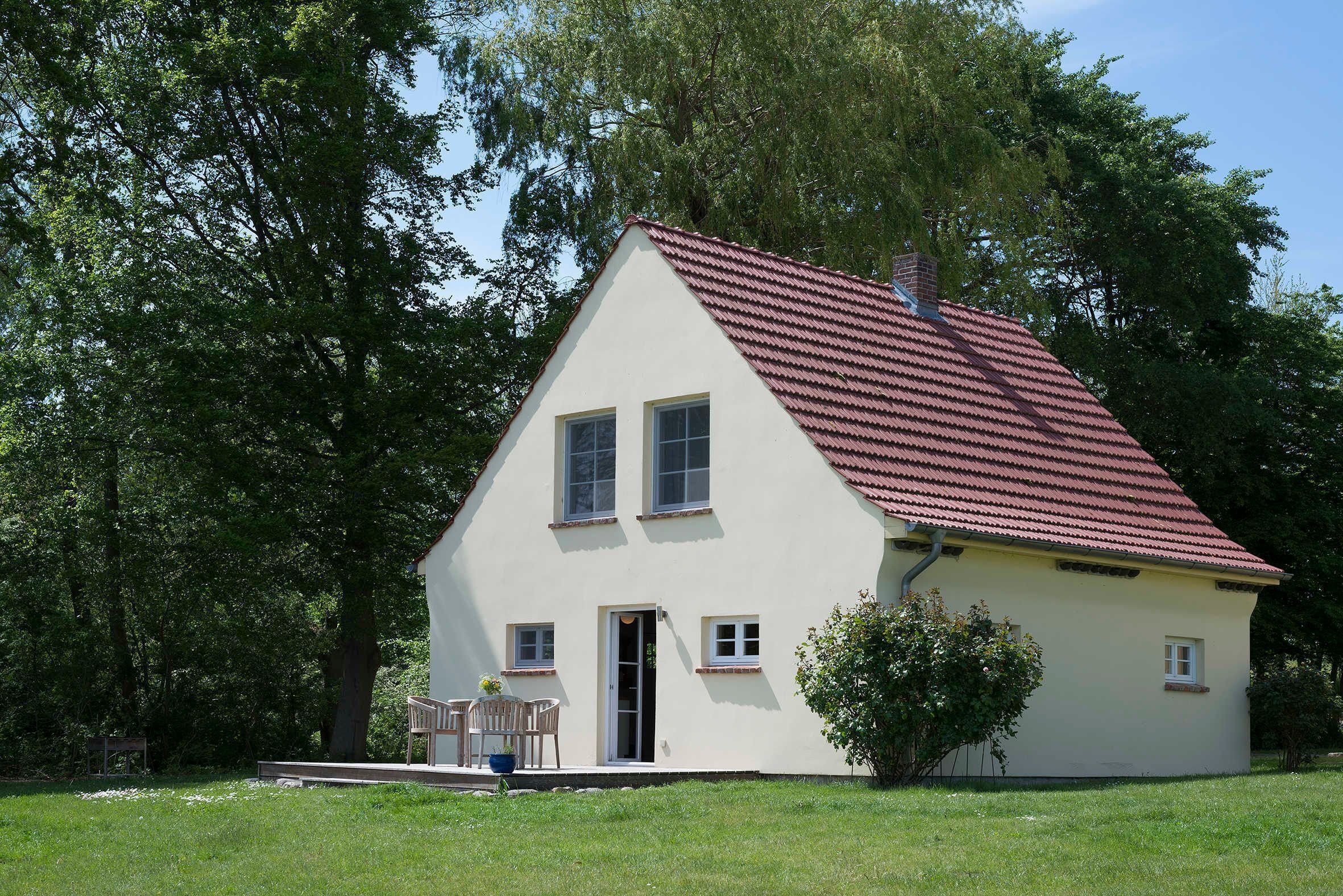 Ett litet, envåningshus med ett rött tegeltak, en ytterdörr och en liten veranda med en stol.