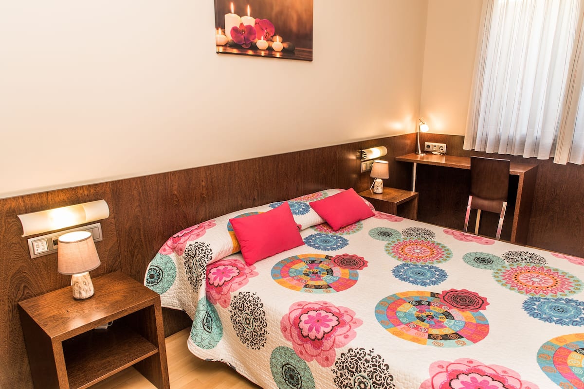 A neatly arranged hotel room with a bed, bedside table, lamp, and a desk with a chair.