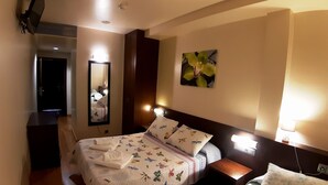A hotel room with a bed, bedside table, nightstand, and a wall-mounted lamp. - Hostal Nirvana (Ponferrada)
