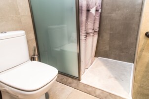 Un baño con inodoro, cabina de ducha de vidrio y cortina de ducha.