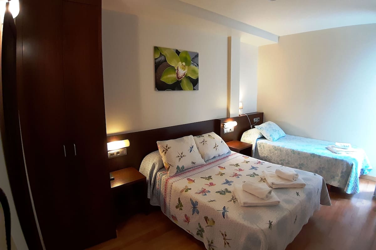 A hotel room with two beds, a nightstand, a wall-mounted lamp, and a painting of flowers.