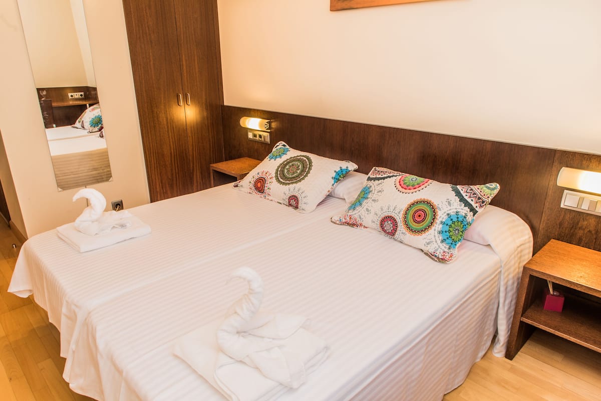 A neatly made bed with white linens, two decorative pillows, and a folded towel on the bed.