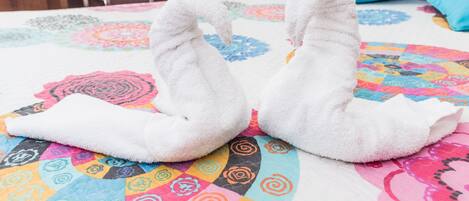 A bed with a colorful quilt and two white towels shaped like swans.