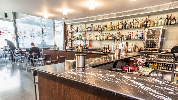 A bar area with a marble countertop, shelves with various bottles, and a seating area with chairs and tables. - Hostal Nirvana (Ponferrada)