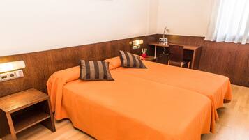 A hotel room with a wooden headboard, an orange bedspread, a bedside table, a lamp, and a desk with a chair.