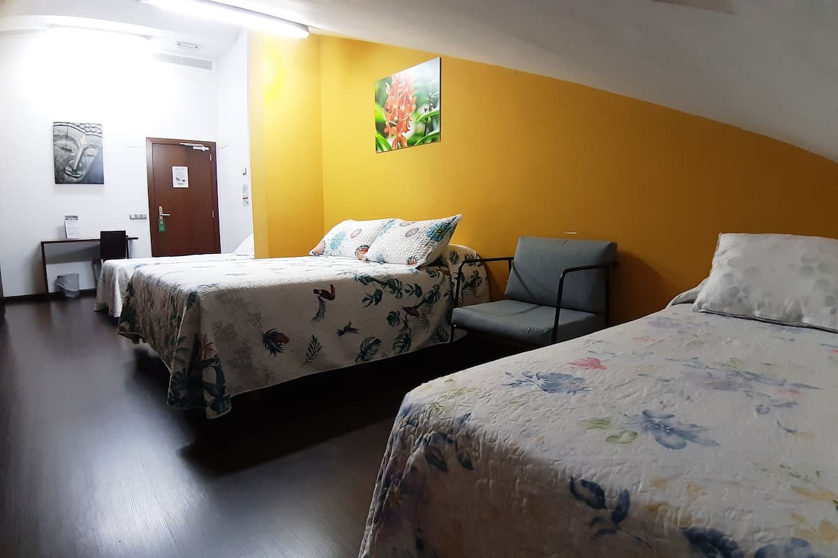 A hotel room with two beds, a chair, a desk, and a door.