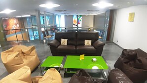 A modern lounge area with leather sofas and bean bags, a green coffee table, and a glass partition. - Hostal Nirvana (Ponferrada)