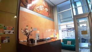 A reception desk with a vase of flowers, a sign reading "Hostal Nirvana," and a glimpse of a green sofa and a glass door leading to a parking area. - Hostal Nirvana (Ponferrada)