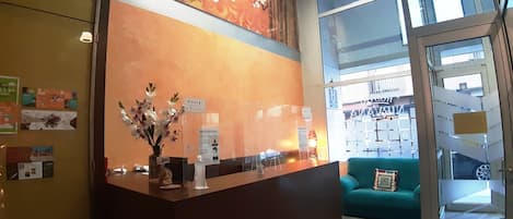 Una recepción con un florero, un letrero que dice "Hostal Nirvana", y se ve un sofá verde y una puerta de vidrio que da a un estacionamiento.