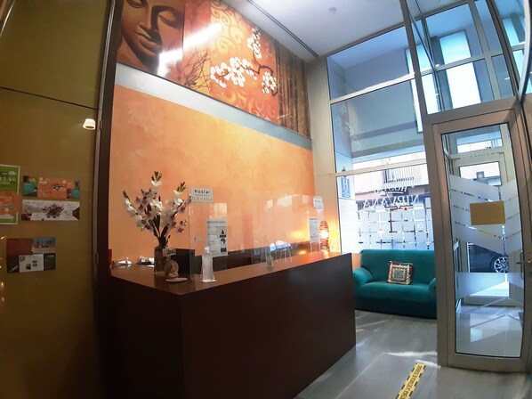 A reception desk with a vase of flowers, a sign reading "Hostal Nirvana," and a glimpse of a green sofa and a glass door leading to a parking area.