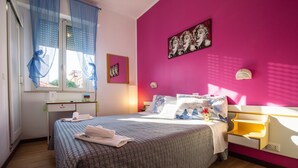 A bedroom with a bed, bedside tables, a window with sheer curtains, and a pink wall with a poster. - Hotel Eriale (Rimini)