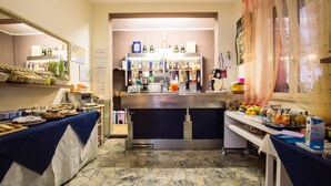 A kitchen area with a bar counter, various food items, and a selection of bottles and glasses. - Hotel Eriale (Rimini)