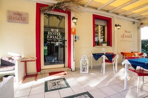 A hotel entrance with a red-framed door, a tiled patio area, and outdoor seating with tables and chairs. - Hotel Eriale (Rimini)