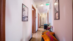 A hotel hallway with framed pictures on the walls, a clock, and a small seating area with a cushion. - Hotel Eriale (Rimini)