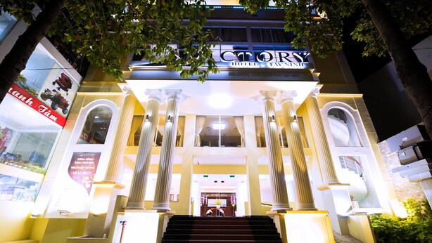 Een hotelentree met grote kolommen, een trap en een bord waarop 'Victory Hotel' staat.