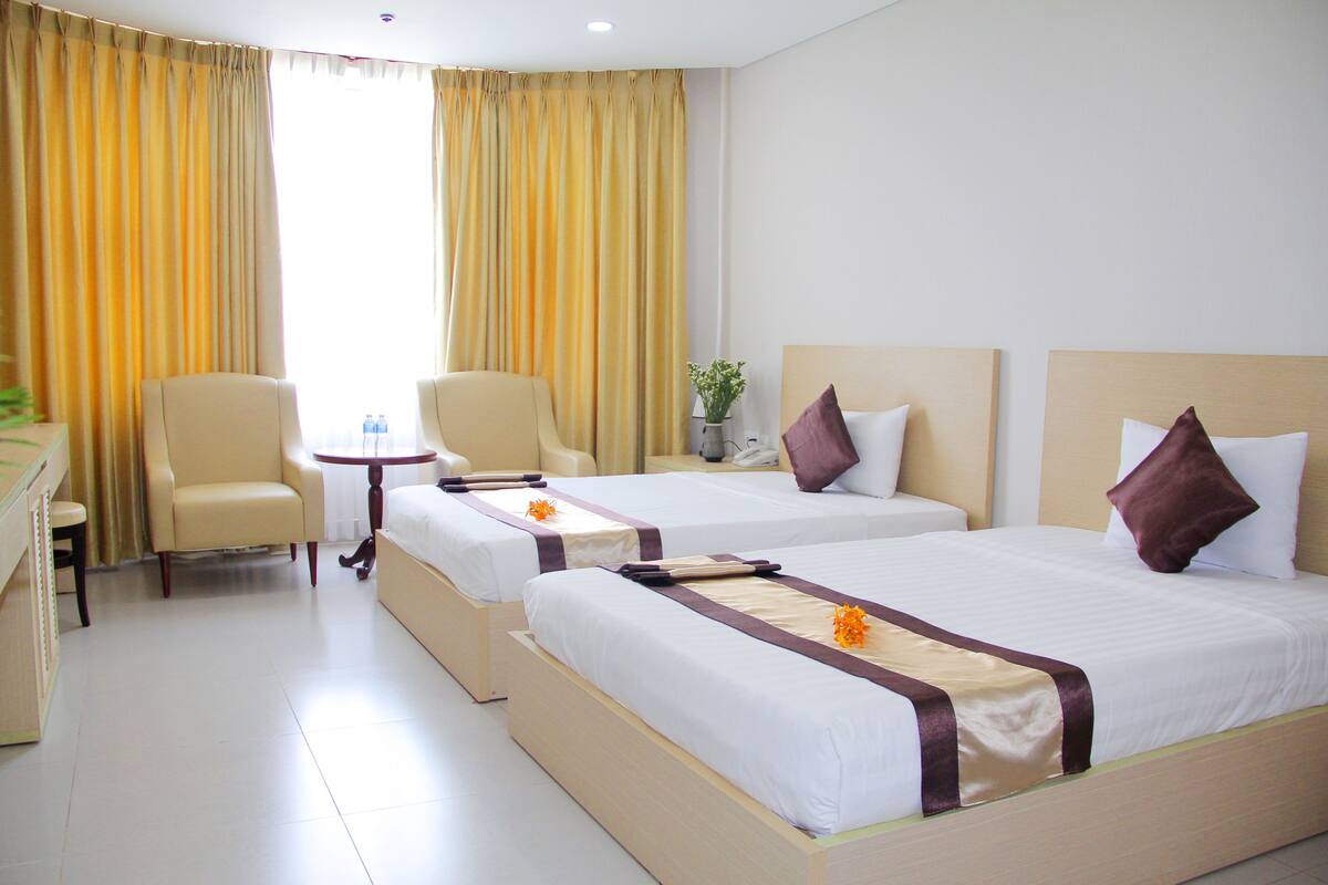 A hotel room with two beds, a sitting area with chairs, a small table, and a window with curtains.