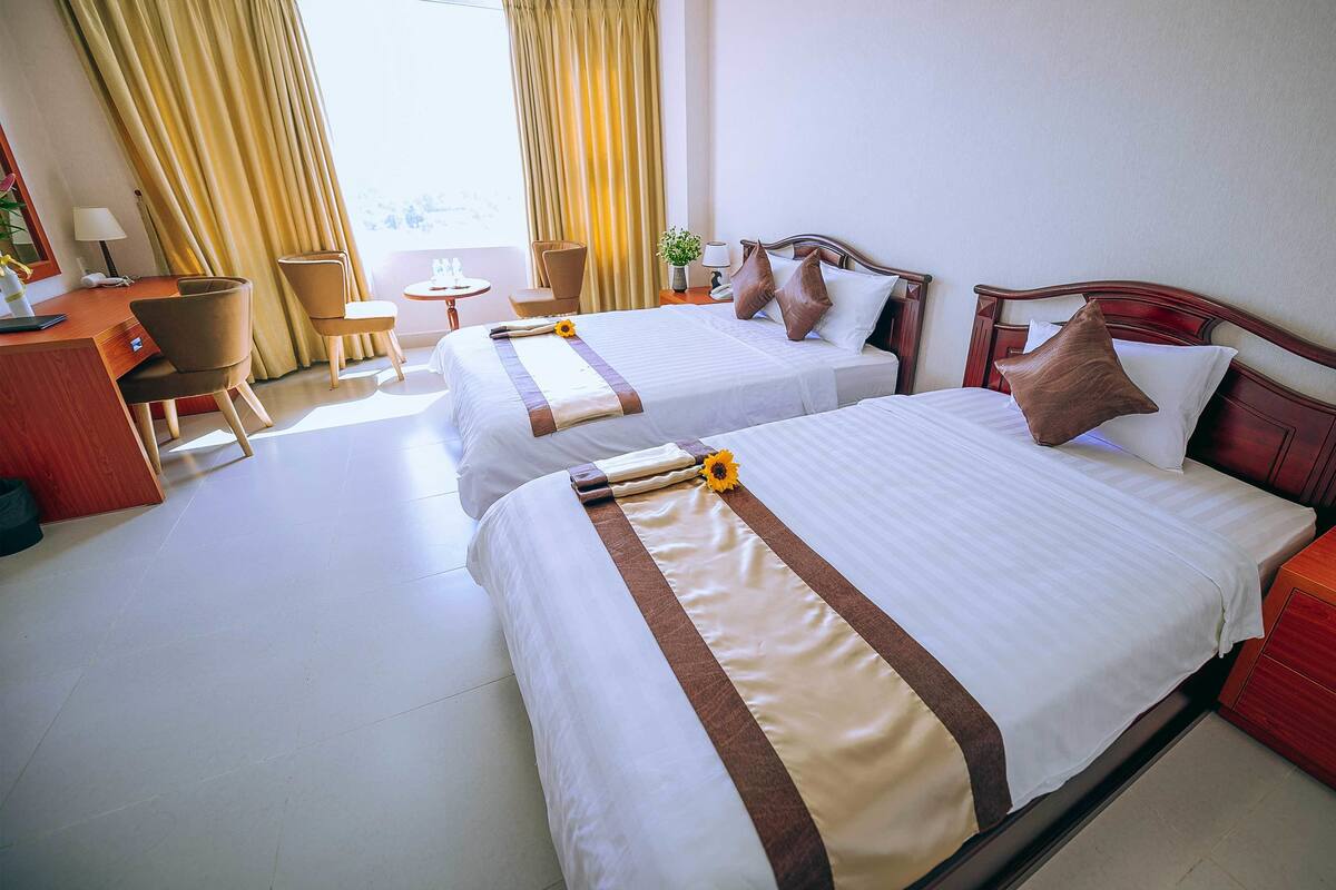 A hotel room with two beds, a desk, a chair, and a small table.