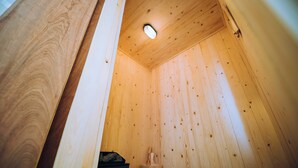 Een houten interieur met een schuine balkenkap, een klein houten bankje en een emmer.