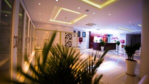 Een moderne hotellobby met een receptiebalie, decoratieve panelen en potplanten.