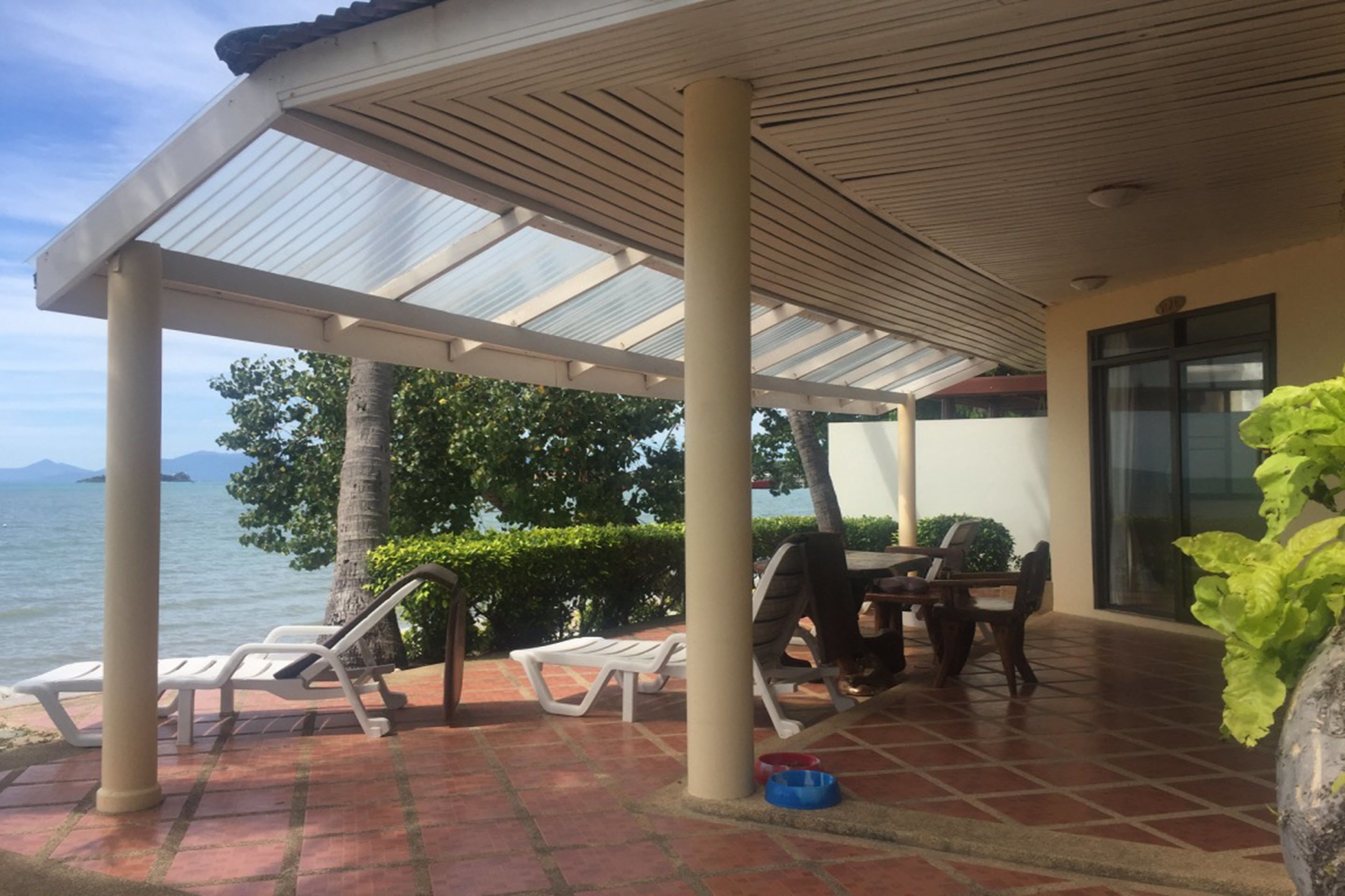 Un patio cubierto con sillones de descanso y una mesa, con vistas a una masa de agua y un paisaje montañoso.